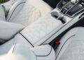 Close-up view of a car’s white leather interior, showing the center console, cup holders, and stitched geometric patterns on the seats and armrest.