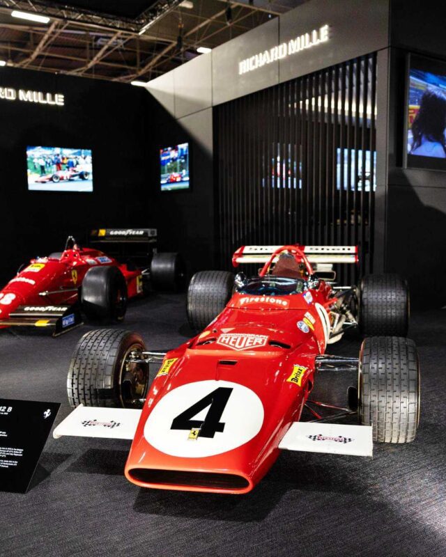 A classic red Formula 1 race car with the number 4 is displayed indoors at Retromobile New York, with another similar car and exhibition signage, highlighting their new strategic partnership, visible in the background.