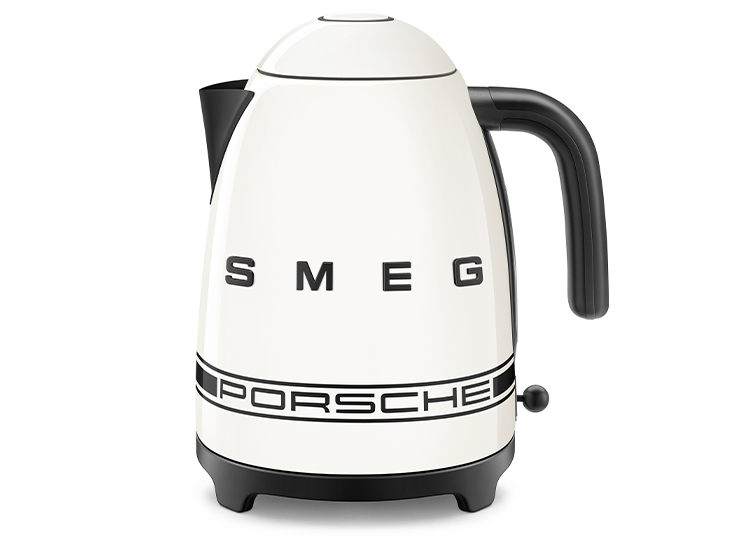 A white electric kettle with a black handle from the SMEG Kitchen Collection, labeled "SMEG" and "PORSCHE" in bold letters on the front.