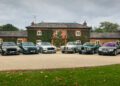 Six legendary sedans are parked in a row on the driveway before a large brick house covered with ivy, including exclusive Bentley Mulliner tributes.