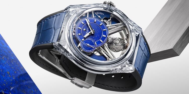 A luxury Zenith DEFY Zero G wristwatch with a blue dial, visible mechanical parts, and a blue leather strap from the Sapphire Collection, displayed on geometric blocks against a white background.