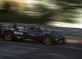 A black Pagani hypercar with gold rims speeds along a racetrack at Auto e Moto d'Epoca 2025, sponsor logos gleaming and motion blur highlighting its power.