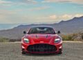 Review: 2025 Aston Martin Vanquish Coupe—a red sports car viewed from the front, parked on a mountain road with hills and a partly cloudy sky in the background.