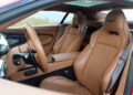 The interior of the 2025 Aston Martin Vanquish Coupe features tan leather seats, modern controls, and the iconic Aston Martin logo on the headrests. Review: luxury meets innovation in every detail.