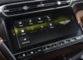 Close-up of a 2025 Aston Martin Vanquish Coupe's touchscreen display with menu options for vehicle, media, navigation, phone, climate, Apple CarPlay, Android Auto, and settings. Review: experience cutting-edge connectivity and control.