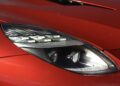 Close-up view of a modern car's sleek headlight on a shiny red vehicle, featured in our Review: 2025 Aston Martin Vanquish Coupe.