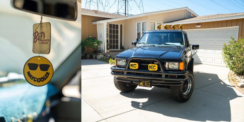 Close-up of a yellow air freshener hanging in a car and a black off-road vehicle with KC lights parked in a suburban driveway, channeling that classic Petrolicious vibe.