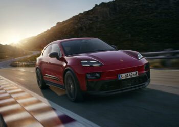 A red 2026 Macan Electric GTS SUV drives on a winding mountain road at sunset, with rocky hills in the background.