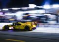A yellow Porsche speeds past blurred lights at night on a racetrack, motion blur highlighting its fast movement in the IMSA WeatherTech series.