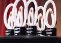 Five modern white and black trophies with circular designs are displayed on a round black table, celebrating the 2025 Porsche Classic Restoration National Winners, set against a blurred gradient background.