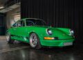 A green Porsche Classic Restoration sports car is parked indoors on a polished concrete floor with a black curtain backdrop.