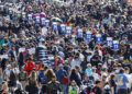 A large crowd gathers on a racetrack, with people holding numbered signs above their heads and many wearing caps and racing attire, ready to cheer for Porsche at the 2025 IMSA WeatherTech SportsCar event.