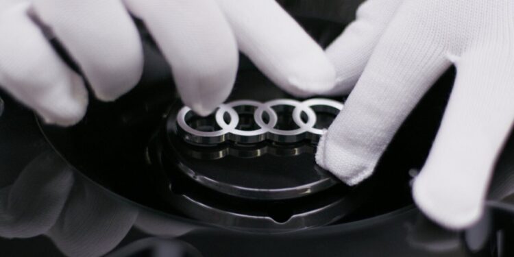 A person wearing white gloves holds a car part featuring the silver Audi logo with four interlinked rings, as seen in a making-of video for a concept car.