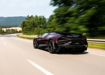 A sleek black Bugatti Mistral speeds down an empty highway bordered by green trees, the blurred background capturing its motion.