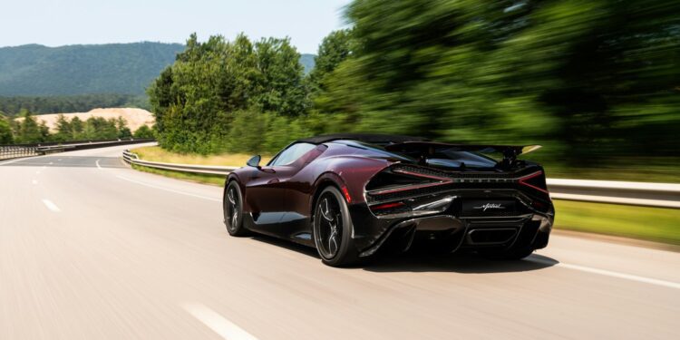 A sleek black Bugatti Mistral speeds down an empty highway bordered by green trees, the blurred background capturing its motion.