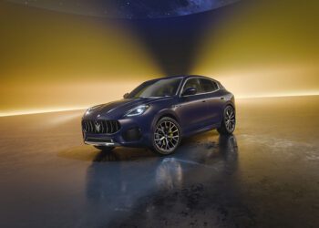 A dark blue Maserati SUV parked on a reflective surface with a gradient yellow and purple background.
