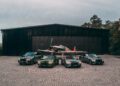 Four luxury cars, including the Bentley Honors Wartime Heroes with the Czech Squadron Collection and 2025 Remembrance Car, are parked in front of a vintage military airplane outside a large black hangar on a paved surface.
