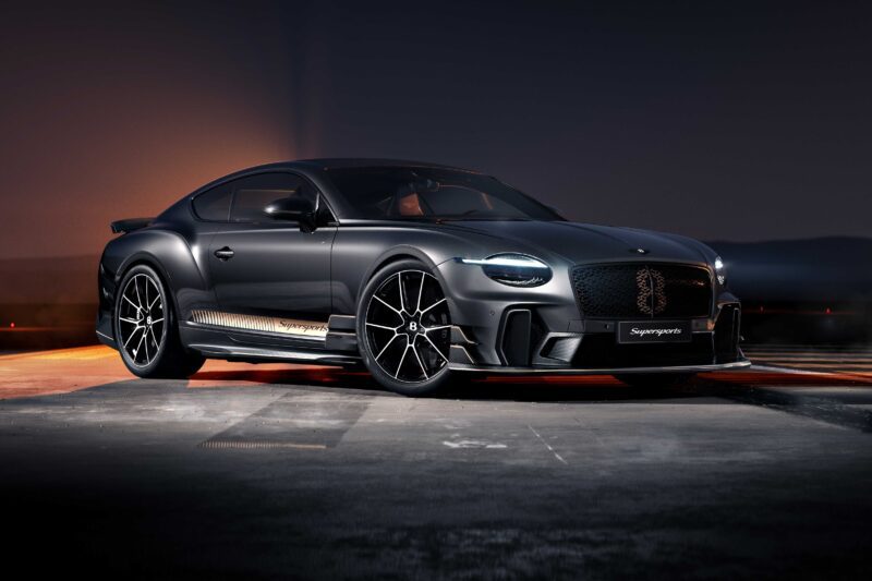 A driver-focused Bentley Supersports, finished in matte black with large alloy wheels and aerodynamic detailing, is parked on a concrete surface at dusk.