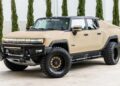 A tan customized Hummer EV truck with large off-road tires is parked on pavement in front of tall green shrubs—an impressive example from Unique Creation Garage's Custom Cars For Sale.