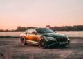 A dark green luxury sports coupe, inspired by Bentley Honors Wartime Heroes with the Czech Squadron Collection and 2025 Remembrance Car, is parked on an open road at sunrise with trees and a misty field in the background.