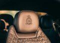 Close-up of a luxury car seat with beige leather upholstery, featuring quilted stitching and an embroidered emblem on the headrest from the Bentley Honors Wartime Heroes with the Czech Squadron Collection.