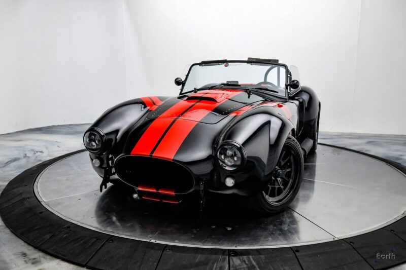 A black vintage convertible sports car with red racing stripes, embodying high-performance style, is parked in a white, circular photo studio.