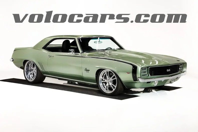 A light green classic Chevrolet Camaro SS coupe, one of the finest classic muscle cars, is displayed in a studio with the "volocars.com" logo in the background.