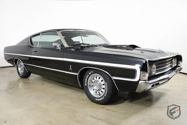 A black classic muscle car with white racing stripes, chrome details, and retro tires, parked indoors on a concrete floor against a white background—a perfect choice for fans of high-performance cars.