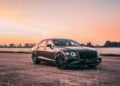 A black luxury sedan, part of the Bentley Honors Wartime Heroes with the Czech Squadron Collection and 2025 Remembrance Car, is parked on a paved surface outdoors at sunset with trees and a colorful sky in the background.
