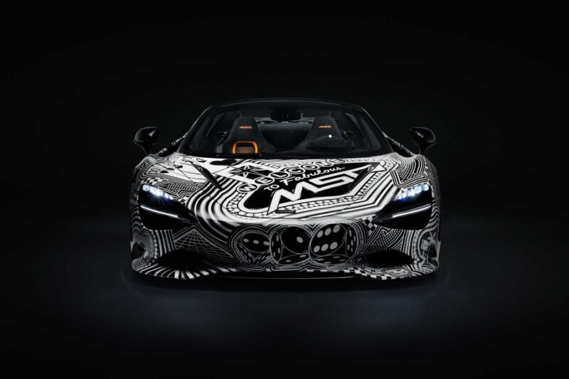 A front view of the Project Viva Revealed: One-of-One McLaren 750S Spider, its exterior wrapped in a black and white geometric and abstract pattern, brings Las Vegas to life against a dark background.