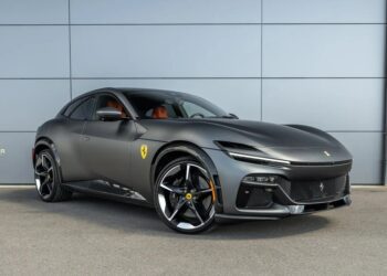 A matte black Ferrari Purosangue SUV parked in front of a gray paneled wall, featuring sporty wheels and yellow Ferrari badges on the front fender and wheel center caps—one of the best SUVs for sale.