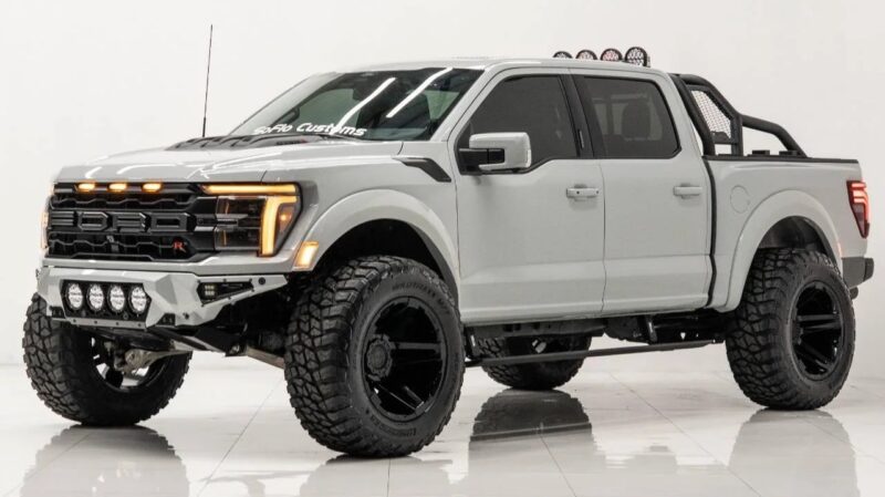 A lifted gray Ford pickup truck with large off-road tires, custom black wheels, front grill lights, roof lights, and a roll bar showcases comfort and capability in a studio setting.