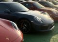 Feature Exclusive: 2025 Icons of Porsche Dubai—several Porsche sports cars are parked closely together in rows on a green surface, with sunlight reflecting off their hoods.