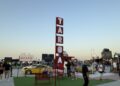 People stroll around a car show area with a tall red "TARGA" sign, vintage cars, benches, and a clear evening sky—Feature Exclusive: 2025 Icons of Porsche Dubai.