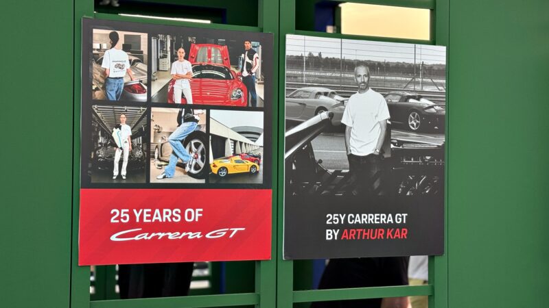 Two posters on a green wall: one says "25 Years of Carrera GT," featuring six car photos; the other reads "25Y Carrera GT by Arthur Kar" with a man by a car. Feature Exclusive: 2025 Icons of Porsche Dubai.