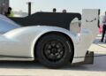 Feature Exclusive: 2025 Icons of Porsche Dubai—close-up side view of a silver Porsche race car’s rear wing and wheel, displayed outdoors with people and buildings in the background.