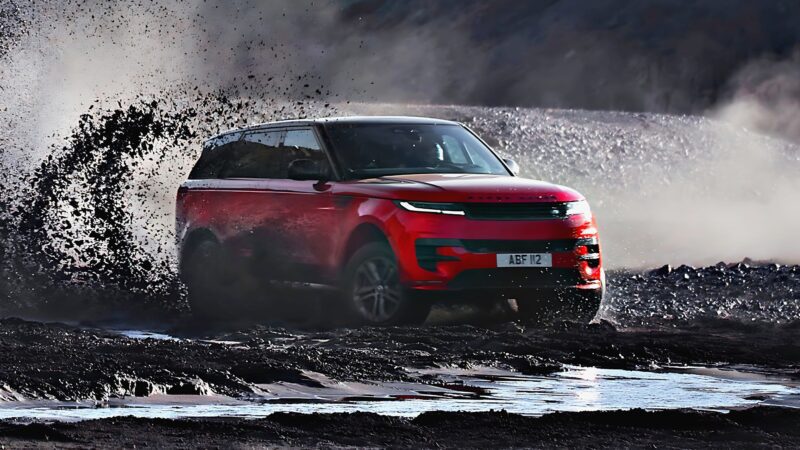 A red SUV, the 2025 Land Rover Range Rover Sport Dynamic SE PHEV, drives through mud and water, splashing dirt to the side and creating a dynamic off-road scene.