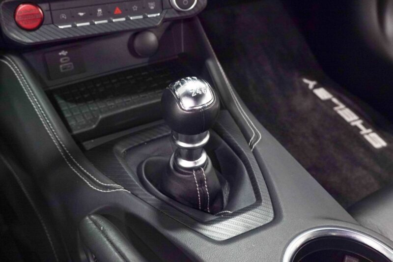 Close-up of a manual gear shift in a car interior with "SHELBY" visible on the floor mat, featured in our Review: 2025 Shelby GT350.