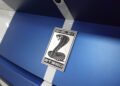 Close-up of a Shelby GT350 badge featuring a cobra emblem on a blue car with white racing stripes. Review: 2025 Shelby GT350 highlights its iconic design and impressive attention to detail.
