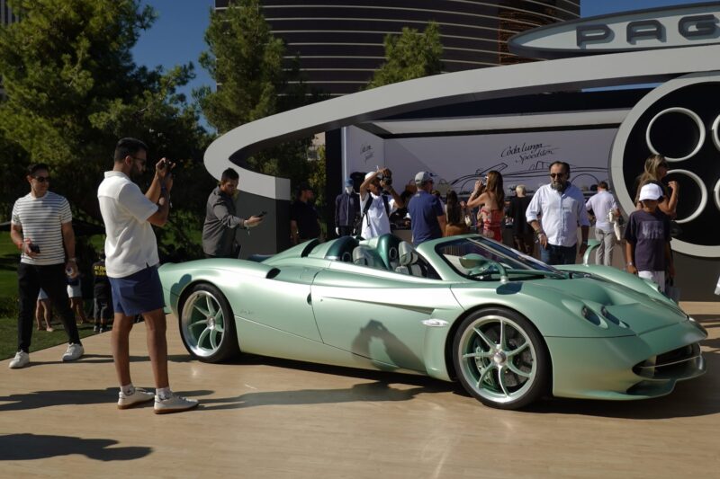 At the Wynn Concours 2025, a group gathers around a light green convertible sports car on display outdoors; one man snaps a photo at Las Vegas’ premier automotive event renowned for hypercars world debuts and elevated hospitality.