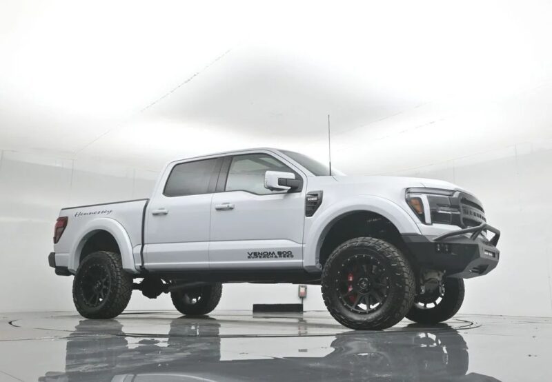 A white Hennessey Venom 800 Ford F-150 pickup truck with large off-road tires exudes style and comfort as it’s parked in a plain, brightly lit studio. Perfect for those who appreciate luxury trucks with bold presence.