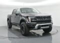 A black Ford F-150 Raptor pickup truck, known for its style and comfort among luxury trucks, is parked in a white, well-lit studio with a circular rotating platform.