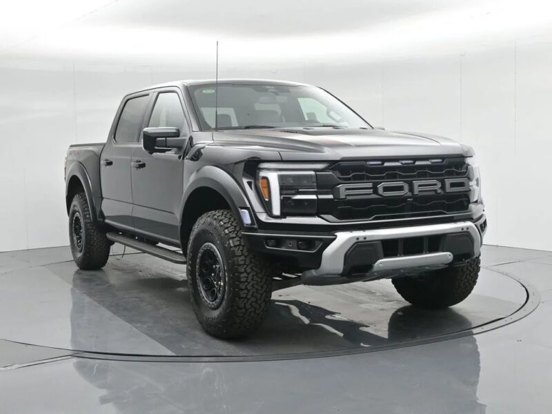 A black Ford F-150 Raptor pickup truck, known for its style and comfort among luxury trucks, is parked in a white, well-lit studio with a circular rotating platform.