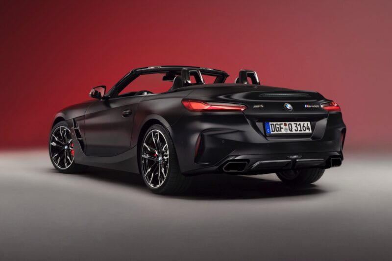 A black BMW Z4 convertible sports car, part of the End of the Road: 2026 BMW Z4 Final Edition Breaks Cover, is parked indoors on a gray floor against a red gradient background, viewed from the rear three-quarters angle.