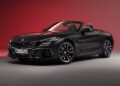 A matte black BMW Z4 convertible sports car is shown in a studio with a red gradient background, highlighting the End of the Road: 2026 BMW Z4 Final Edition Breaks Cover in bold, striking style.