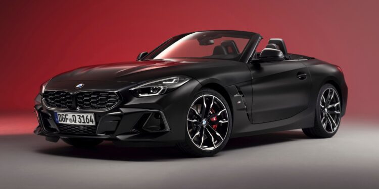 A matte black BMW Z4 convertible sports car is shown in a studio with a red gradient background, highlighting the End of the Road: 2026 BMW Z4 Final Edition Breaks Cover in bold, striking style.