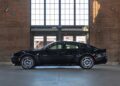 A powerful sedan in black is parked indoors, set against large windows and a brick wall.