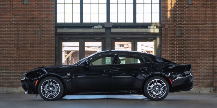 A powerful sedan in black is parked indoors, set against large windows and a brick wall.