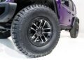 Close-up view of a large BFGoodrich all-terrain tire and black alloy wheel on a purple off-road vehicle, part of the First of 12: Jeep Launches Its 85th Anniversary Limited Edition Series With the Moab 392, shown on a white background.