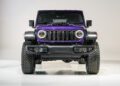 Front view of a purple Jeep Moab 392 off-road vehicle, featuring large tires, round headlights, and a seven-slot grille—part of Jeep’s 85th Anniversary Limited Edition Series—photographed in a studio setting.
